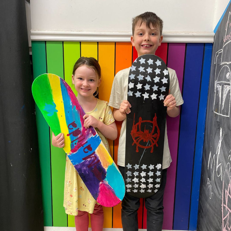 Two children holding colorful skateboard deck from a skateboard deck party at DIY Invasion