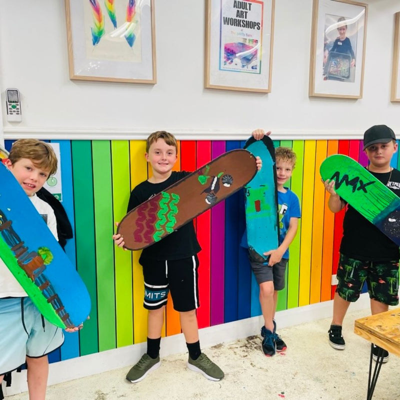 Four children holding colorful skateboards in DIY Invasion workshop room