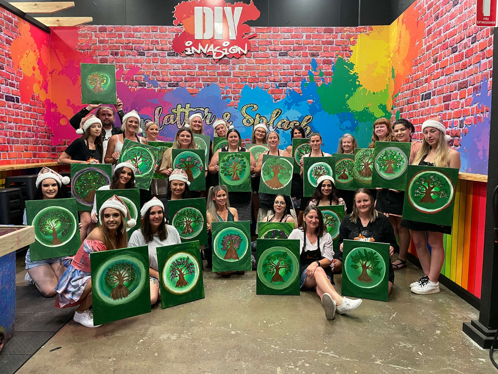 A group of Childcare Workers posing for a photo with the newly completed 'Tree of Life' Paintings they did in our Paint n Sip Team Building Night