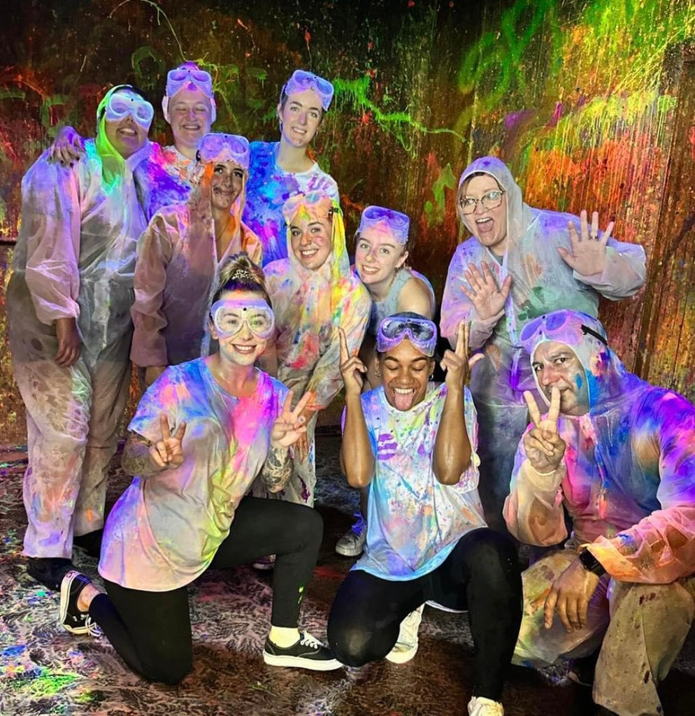 A group of workers having fun posing in our Splash Room covered in paint.